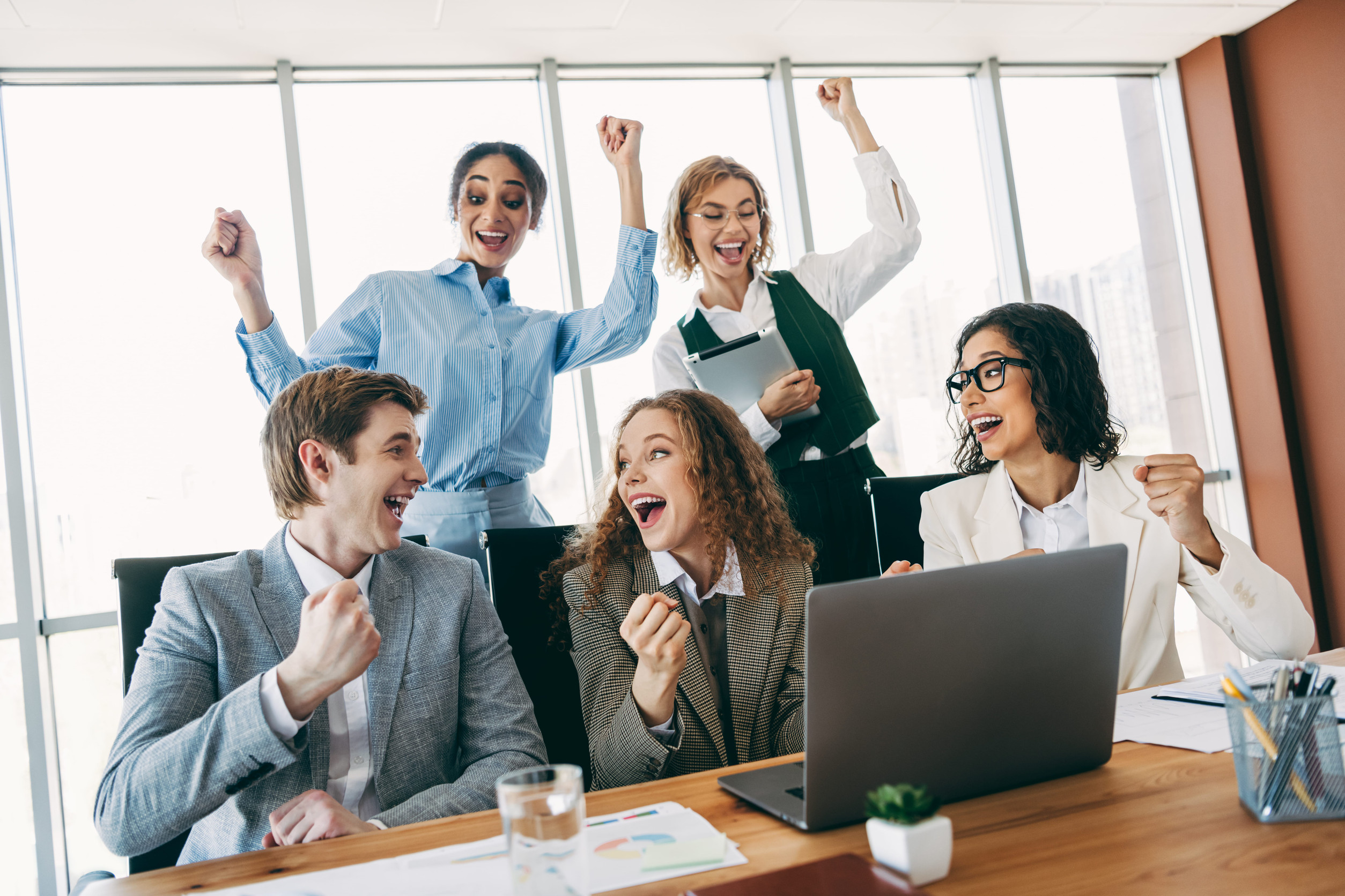 Business team celebrating around a laptop during a meeting, illustrating successful marketing execution, improved efficiency through automation, team collaboration, and business growth.

